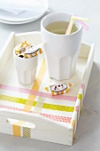Beaker, drinking straws and toffees on tray decorated with washi tape