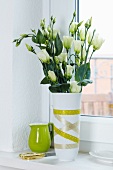 White Texas bluebells (Eustoma grandiflorum) in vase decorated with green masking tape; lime green china jug in background