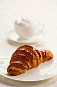 A croissant on a plate with a cappuccino in the background