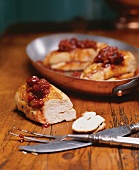 Chicken Breasts Topped with a Cherry Rhubarb Chutney; One Cut on Wooden Table; Some in Pan; Carving Set