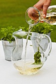 White wine being poured into a jug of woodruff