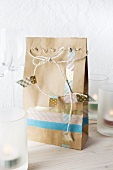 A paper bag decorated with masking tape and white string between glasses and candles