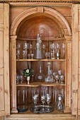 Glass collection in ornately carved cabinet with rounded arch