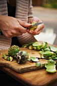 Woman Using a Knife to Peel Baby Artichokes Over a Wooden Cutting Board