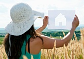 Woman holding up cut-out paper silhouette of house against landscape