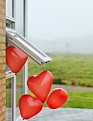 Herzförmige Luftballons fliegen aus einem Fenster