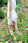 Young woman standing in field of zinnias, holding apple, cropped