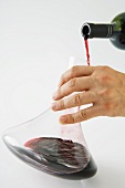 Man pouring red wine into decanter, cropped view of hand
