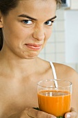 Woman holding glass of vegetable juice, frowning at camera