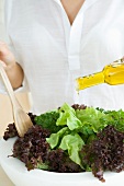 Woman preparing salad, pouring olive oil dressing