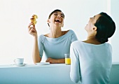 Two women on either side of bar having breakfast, laughing