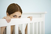 Woman peeking over side of crib at camera