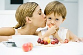 Woman kissing little boy on cheek, boy eating apple