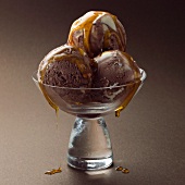Three scoops of chocolate ice cream with syrup in a glass bowl