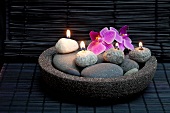 Meditative atmosphere in spa - orchid flowers and lit pebble candles in stone dish