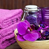 Violet still-life in spa room - orchid flowers in bamboo dish next to stacked towels