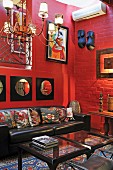 Corner of living room with African artworks on red-painted brick wall above leather sofa