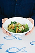 A person holding a bowl of spicy fish salad (Asia)