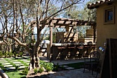 Sonniger Terrassenplatz im Garten mit gemauerter Bar unter Pergola und rustikalem Kamin