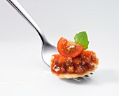 Ravioli filled with tomatoes and minced meat with sauce and a basil leaf on a fork