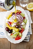 A Greek salad being drizzled with olive oil