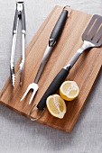 Barbecue utensils and a lemon on a chopping board