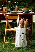 Bag of baguettes hanging on chair back in front of set table in garden