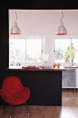Red armchair against black wall with opening and built-in breakfast bar showing view of open-plan, designer kitchen