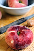 Ein flacher Pfirsich mit Messer auf Holzbrett