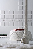 White, vintage metal column in front of pouffe and white square elements on wall