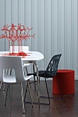 Stylised coral ornament on table and modern chairs in front of white wooden wall