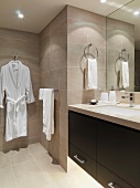 Badezimmerecke - Waschtisch mit schwarzem Unterschrank vor Spiegel und Bademantel vor gefliester Wand aufgehängt
