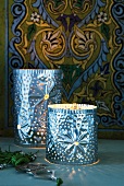 Oriental metal candle lanterns punched with patterns of holes in front of painted wooden panel