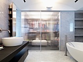 Moderner Waschtisch und freistehende Badewanne vor integrierter Ankleide mit geschlossenen Glasschiebetüren