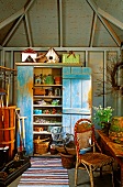 Pastel-coloured, vintage wooden cupboard, gardening utensils and plant pots inside garden shed