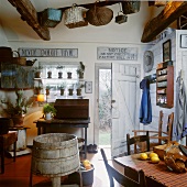 Rustic kitchen with simple board door, collection of baskets hanging from ceiling and vintage dining table with simple wooden chairs