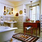 Nostalgisches Badezimmer mit antikem Waschtisch, einem Standwaschbecken, einer freistehenden Badewanne mit goldenen Füssen und blau-weissen Wandfliesen