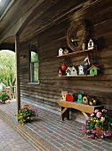 Wooden house with bench, flower arrangements and collection of bird boxes on roofed veranda, 