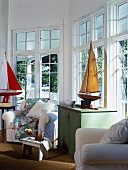 Maritimes Wohnzimmer mit Modell-Segelbooten, weissen Sesseln und einer großen Fensterfront