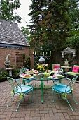 Garden terrace with delicate, pastel blue garden chairs around round glass table with pastel green metal legs