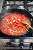 A pan of tomato sauce with bacon on a gas hob