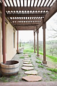 Pathway of rough stone slabs below pergola running along house with view of countryside
