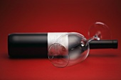 A wine bottle and a wine glass lying against a red background