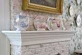 Collection of antique teapots on mantelpiece against brick chimney breast