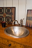 Old, hammered metal wash basin with vintage tap fitting in wooden base unit