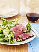 Sliced Beef Over Lettuce with a Creamy Dressing; Glass of Red Wine