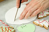 Biscuit decorations being cut out of fondant with decorated Christmas tree biscuits next to it