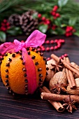 An orange pierced with clove tied with a pink ribbon with walnuts and spices