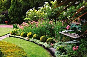 Schattenplatz mit Gartenbank in prächtig blühendem Garten mit gepflegtem Rasen