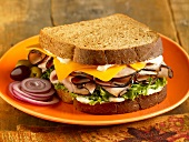 Turkey and Cheese Sandwich on Toasted Wheat Bread; Onion Slices and Olives; On a Plate